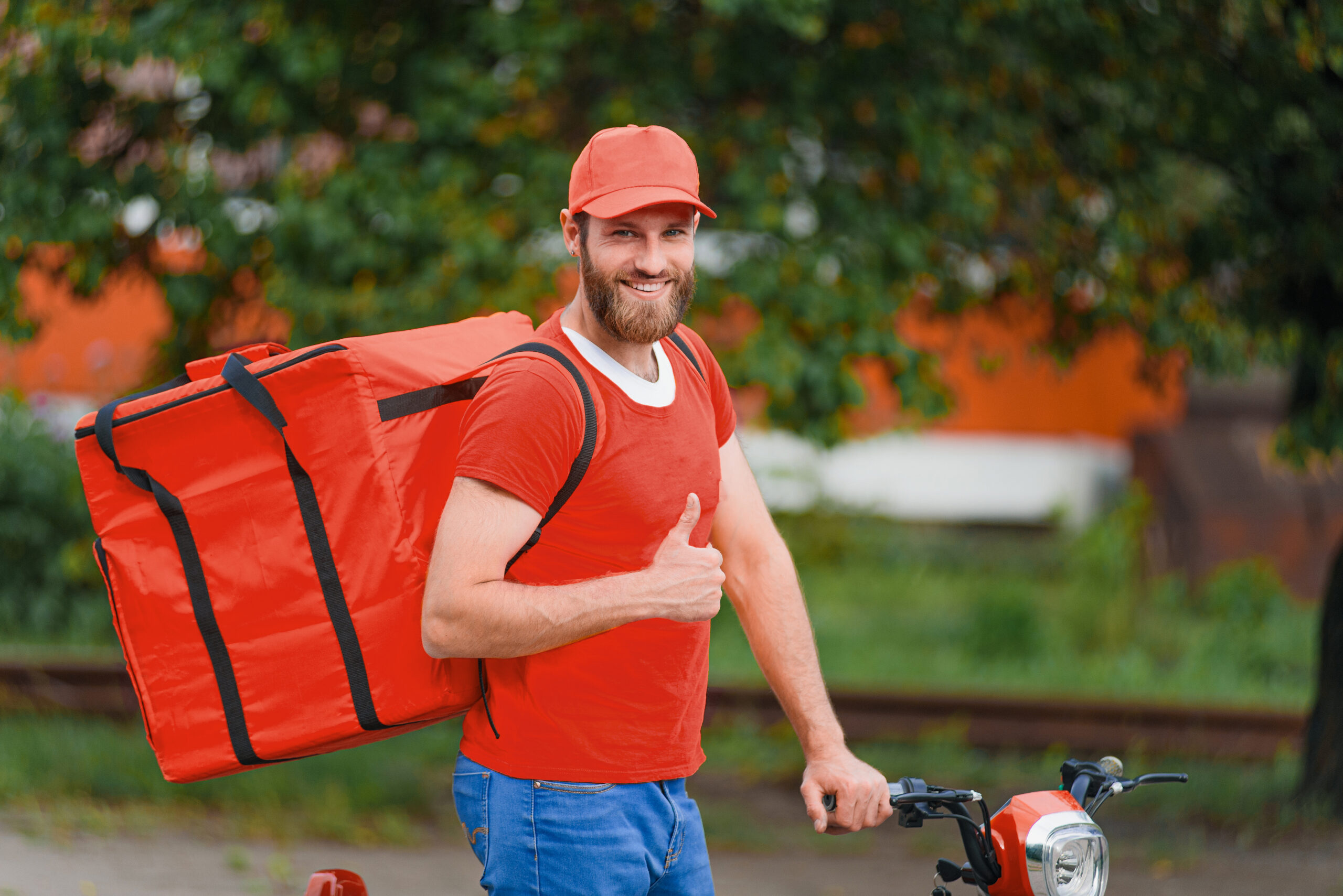 Food delivery man in red uniform with food delivery bag on his back smiling and showing thumb up