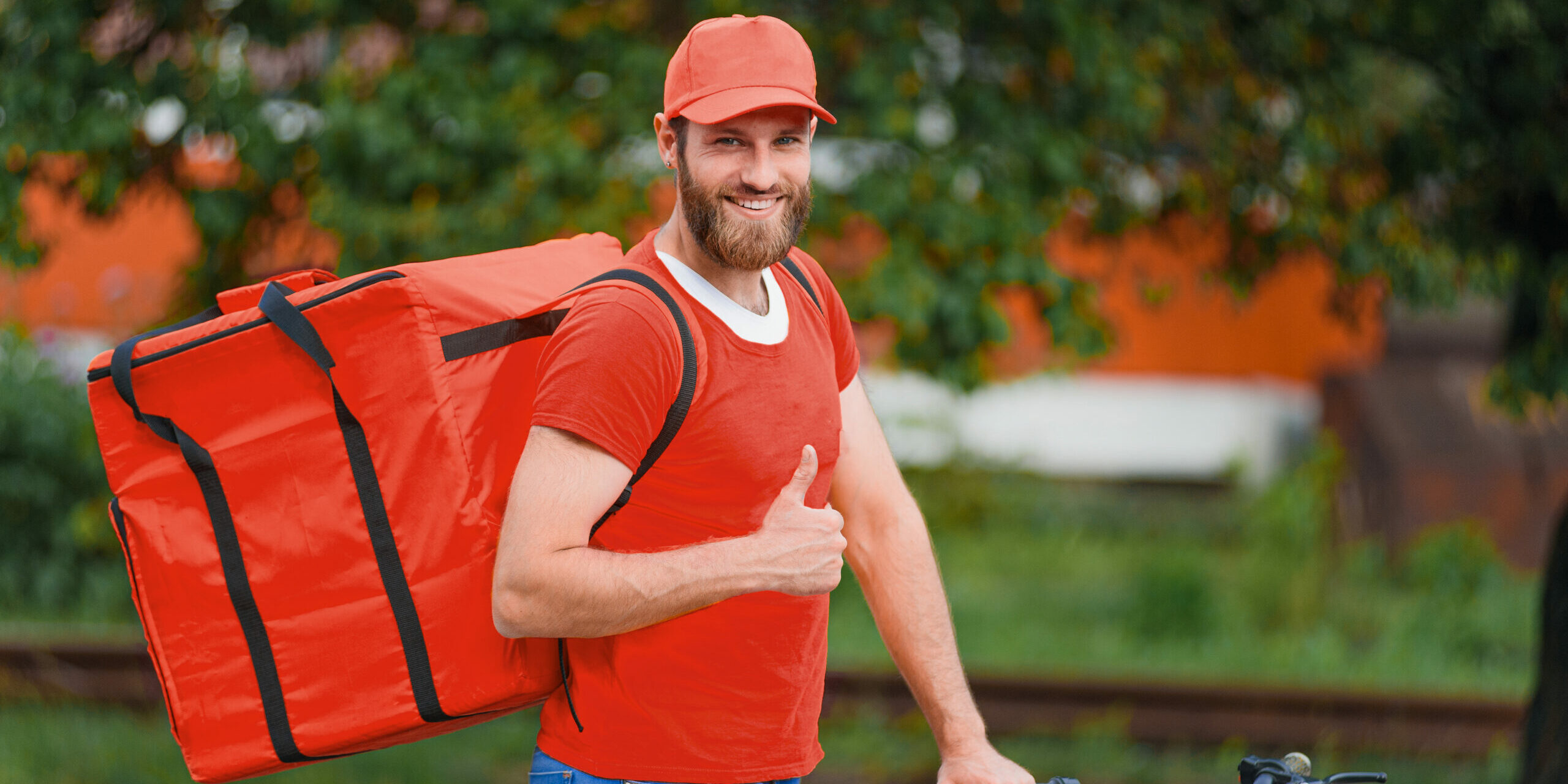 Food delivery man in red uniform with food delivery bag on his back smiling and showing thumb up